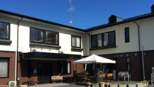 介護施設の建物外観。中庭にテーブルと椅子が配置された屋外スペース
