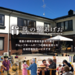 施設の外観。看板と入口周辺に人物が集まっている様子